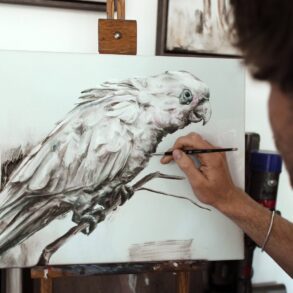 man painting parrot with reference