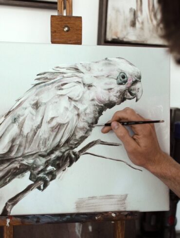 man painting parrot with reference