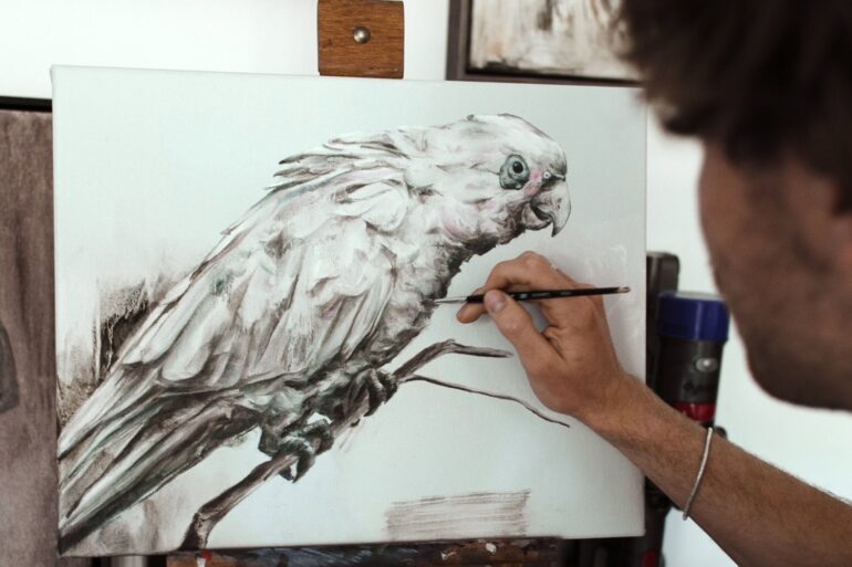 man painting parrot with reference